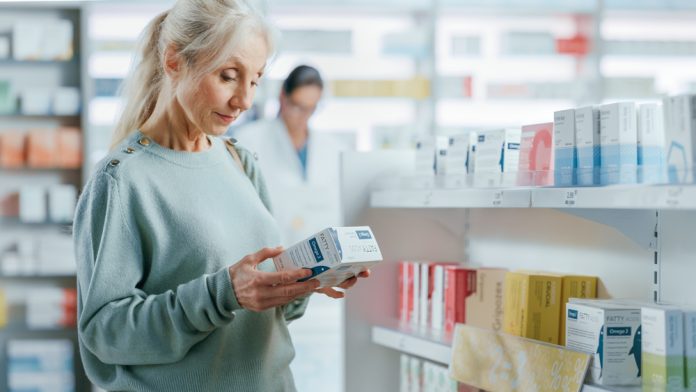 Pharmacy Drugstore: Portrait of a Beautiful Senior Woman Choosing to Buy Medicine, Drugs, Vitamins. Apothecary Full of Health Care Products, Supplement Bottles, Beauty Packages with Modern Design